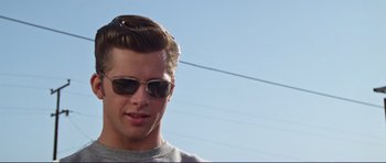 Movie still from “Grease 2” (1982), directed by Patricia Birch – A young man wearing sunglasses and a gray shirt; Close Up shot, Low angle