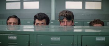 Movie still from “Grease 2” (1982), directed by Patricia Birch – A couple of men standing next to each other in a room; Medium shot, Low angle