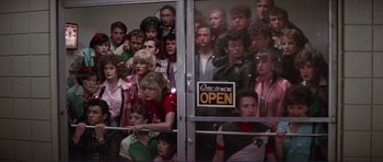 Movie still from “Grease 2” (1982), directed by Patricia Birch – A group of people standing in front of an open door; Wide shot, High angle