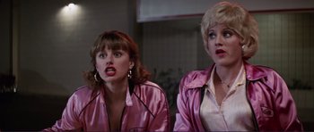 Movie still from “Grease 2” (1982), directed by Patricia Birch – A couple of people that are standing up in a room; Medium shot, Over the shoulder angle