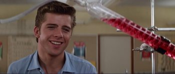 Movie still from “Grease 2” (1982), directed by Patricia Birch – A young man smiling for the camera in a room; Close Up shot, Over the shoulder angle