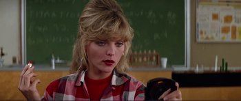 Movie still from “Grease 2” (1982), directed by Patricia Birch – A woman in a plaid shirt looking at her cell phone in front of a chalkboard; Close Up shot, Over the shoulder angle