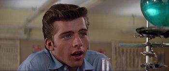 Movie still from “Grease 2” (1982), directed by Patricia Birch – A young man sitting at a table with a glass; Close Up shot, Over the shoulder angle