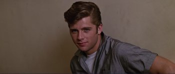 Movie still from “Grease 2” (1982), directed by Patricia Birch – A young man with short brown hair wearing a gray shirt; Close Up shot, Over the shoulder angle
