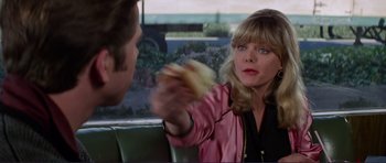 Movie still from “Grease 2” (1982), directed by Patricia Birch – A woman holding a sandwich in front of a man in a car; Medium shot, Over the shoulder angle