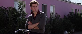 Movie still from “Grease 2” (1982), directed by Patricia Birch – A young man standing in front of a purple building; Medium shot, Over the shoulder angle