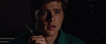 Movie still from “Grease 2” (1982), directed by Patricia Birch – A young man holding a cell phone up to his ear; Close Up shot, Over the shoulder angle