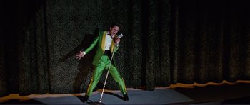 Movie still from “Grease 2” (1982), directed by Patricia Birch – A man wearing a green suit and holding a microphone on a stage; Wide shot, Low angle