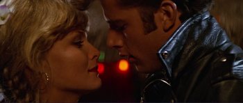 Movie still from “Grease 2” (1982), directed by Patricia Birch – A man and a woman kissing in front of a red light at night; Close Up shot, Over the shoulder angle