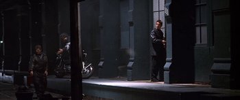 Movie still from “Great Expectations” (1998), directed by Alfonso Cuarón – A man in a black suit standing in front of a building; Wide shot, Low angle