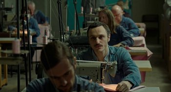 Movie still from “Great Freedom” (2021), directed by Sebastian Meise – A group of people sitting around a sewing machine in a room; Medium shot, High angle