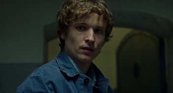 Movie still from “Great Freedom” (2021), directed by Sebastian Meise – A young man with long blonde hair wearing a blue jacket; Close Up shot, Over the shoulder angle