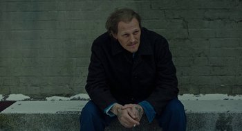 Movie still from “Great Freedom” (2021), directed by Sebastian Meise – A man sitting on the side of the road with his hands crossed; Medium shot, High angle