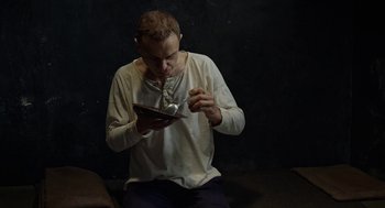 Movie still from “Great Freedom” (2021), directed by Sebastian Meise – A man sitting on the ground looking at a book; Medium shot, High angle
