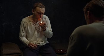 Movie still from “Great Freedom” (2021), directed by Sebastian Meise – A man sitting on the ground with a candle in his mouth; Medium shot, High angle