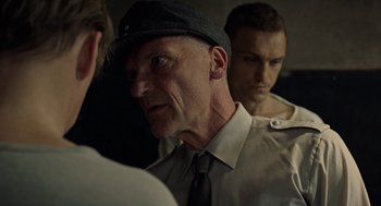 Movie still from “Great Freedom” (2021), directed by Sebastian Meise – A man wearing a hat and a tie looking into a mirror; Close Up shot, Over the shoulder angle