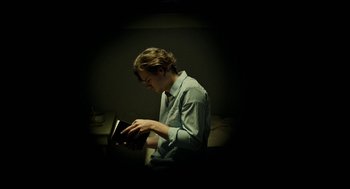 Movie still from “Great Freedom” (2021), directed by Sebastian Meise – A young man reading a book in a dark room; Medium shot, Low angle