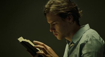 Movie still from “Great Freedom” (2021), directed by Sebastian Meise – A young man reading a book in a dark room; Close Up shot, Low angle