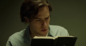 Movie still from “Great Freedom” (2021), directed by Sebastian Meise – A young man reading a book in a dark room; Close Up shot, Low angle