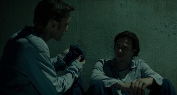Movie still from “Great Freedom” (2021), directed by Sebastian Meise – Two men are sitting on the ground and one is holding a jacket; Medium shot, Over the shoulder angle