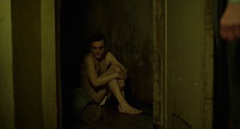 Movie still from “Great Freedom” (2021), directed by Sebastian Meise – A man sitting on the ground in a dark room; Medium shot, High angle