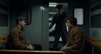 Movie still from “Great Freedom” (2021), directed by Sebastian Meise – Two men are sitting on a train while a man in a uniform stands in the doorway; Medium shot, Over the shoulder angle