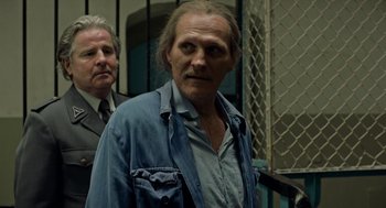 Movie still from “Great Freedom” (2021), directed by Sebastian Meise – A man in a blue jacket standing next to another man in a black suit; Close Up shot, Over the shoulder angle