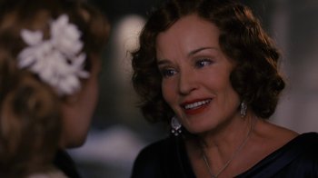 An older woman wearing a necklace and a flower in her hair talking to a younger woman