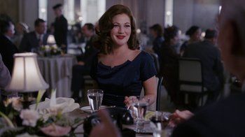 Movie still from “Grey Gardens” (2009), directed by Michael Sucsy – A woman sitting at a table with a glass of water; Medium shot, Over the shoulder angle