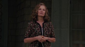 Movie still from “Grey Gardens” (2009), directed by Michael Sucsy – A woman standing in front of a building with her hands clasped together; Medium shot, Low angle