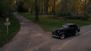 Movie still from “Grey Gardens” (2009), directed by Michael Sucsy – An old car is parked on the side of the road; Extreme Wide shot, High angle