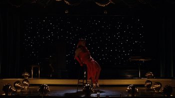 Movie still from “Grey Gardens” (2009), directed by Michael Sucsy – A woman sitting on top of a chair on a stage; Wide shot, High angle