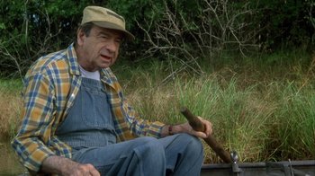 Movie still from “Grumpier Old Men” (1995), directed by Howard Deutch – An older man sitting on the ground holding a cigar; Medium shot, High angle