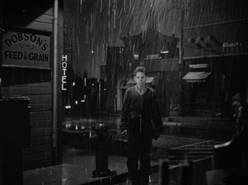 Movie still from “Gun Crazy” (1950), directed by Joseph H. Lewis – A man standing in the rain in front of a hotel; Wide shot, High angle