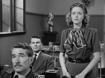 Movie still from “Gun Crazy” (1950), directed by Joseph H. Lewis – A man and a woman sitting in front of another man in front of a window; Medium shot, Low angle