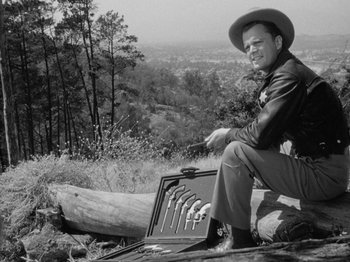 Movie still from “Gun Crazy” (1950), directed by Joseph H. Lewis – A black and white photo of a man sitting on the ground; Medium shot, Low angle