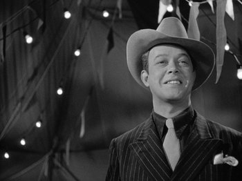 Movie still from “Gun Crazy” (1950), directed by Joseph H. Lewis – A black and white photo of a man wearing a suit and a hat; Medium shot, Low angle
