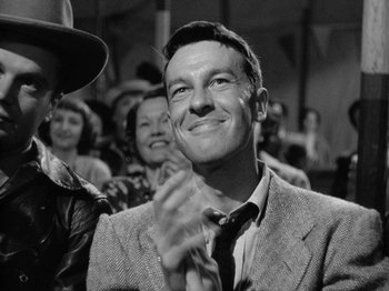 Movie still from “Gun Crazy” (1950), directed by Joseph H. Lewis – A man in a suit and tie clapping in front of a group of people; Close Up shot, Over the shoulder angle