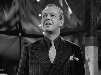 Movie still from “Gun Crazy” (1950), directed by Joseph H. Lewis – A man wearing a suit and tie standing in front of an umbrella; Close Up shot, Low angle