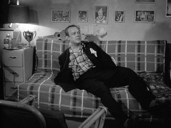 Movie still from “Gun Crazy” (1950), directed by Joseph H. Lewis – A black and white photo of a man sitting on a couch; Medium shot, High angle