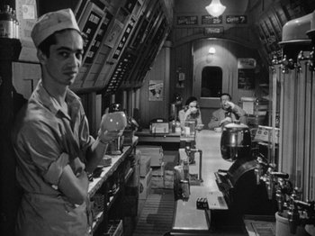 Movie still from “Gun Crazy” (1950), directed by Joseph H. Lewis – A group of men standing around a kitchen; Medium shot, Low angle