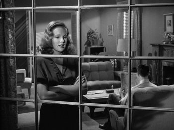 Movie still from “Gun Crazy” (1950), directed by Joseph H. Lewis – A woman standing in front of another woman in a living room; Medium shot, Over the shoulder angle