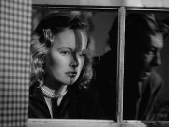 Movie still from “Gun Crazy” (1950), directed by Joseph H. Lewis – A black - and - white photo of a woman looking out of a window; Close Up shot, Over the shoulder angle