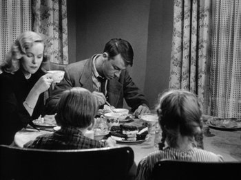 Movie still from “Gun Crazy” (1950), directed by Joseph H. Lewis – An old black and white photo of a family sitting at a dinner table; Medium shot, Low angle