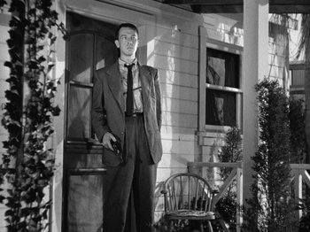Movie still from “Gun Crazy” (1950), directed by Joseph H. Lewis – A man standing in front of a house holding a gun; Medium shot, Low angle