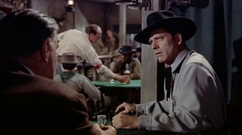 Movie still from “Gunfight at the O.K. Corral” (1957), directed by John Sturges – A man sitting at a table in a room; Medium shot, Over the shoulder angle