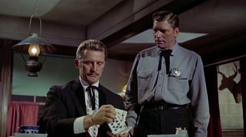 Movie still from “Gunfight at the O.K. Corral” (1957), directed by John Sturges – A man in a suit and tie playing cards with another man in a uniform; Medium shot, Over the shoulder angle