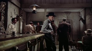 Movie still from “Gunfight at the O.K. Corral” (1957), directed by John Sturges – A man in a cowboy hat standing at a bar; Wide shot, Low angle