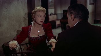 Movie still from “Gunfight at the O.K. Corral” (1957), directed by John Sturges – A woman in a red dress sitting next to a man in a black suit; Medium shot, Over the shoulder angle