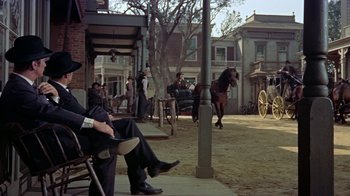 Movie still from “Gunfight at the O.K. Corral” (1957), directed by John Sturges – A man sitting on a chair in a yard; Wide shot, Low angle